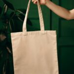 Simple cotton tote bag held by a hand against a green background, ideal for eco themes.