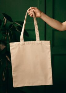Simple cotton tote bag held by a hand against a green background, ideal for eco themes.